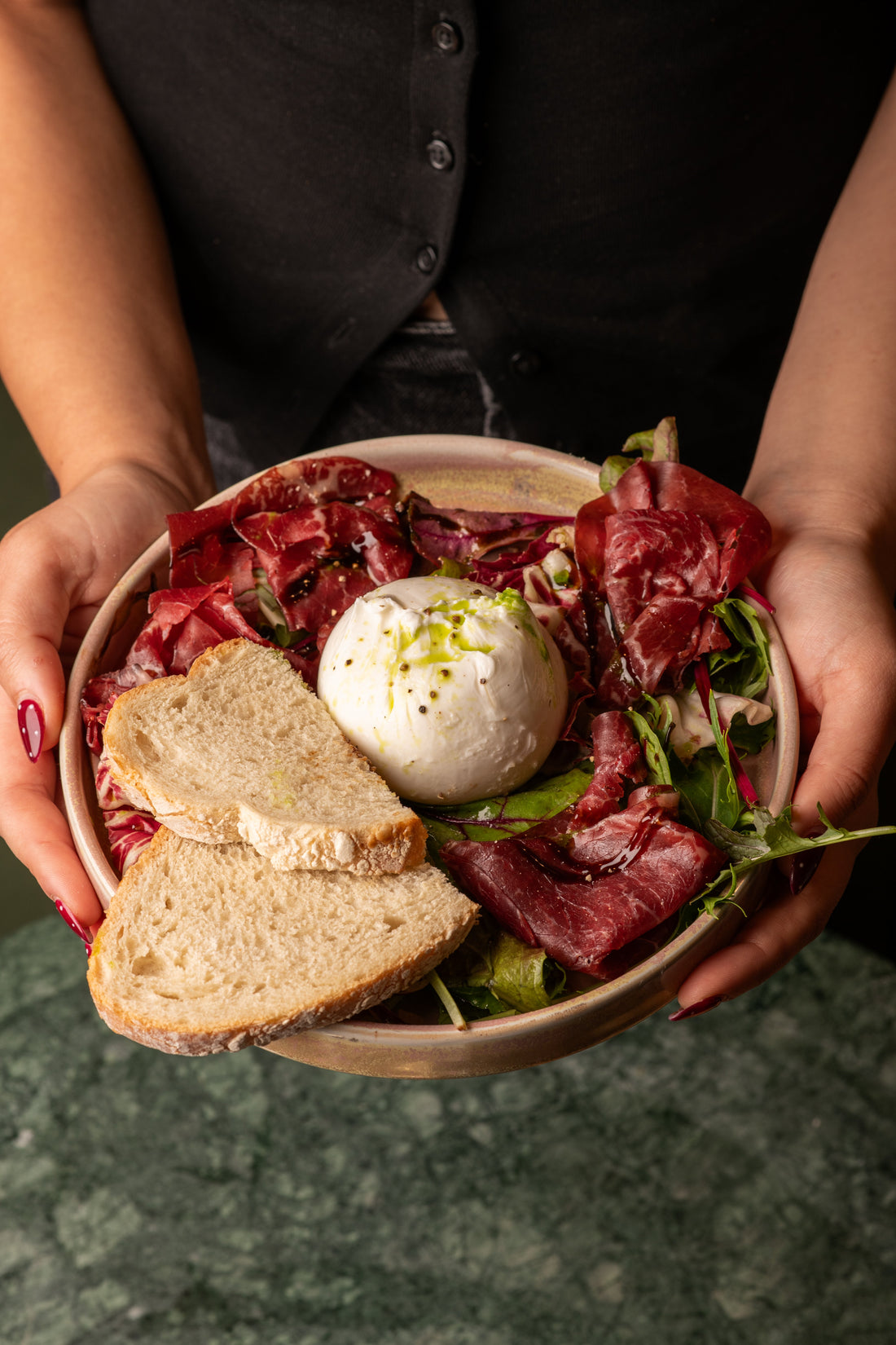 Bresaola and burrata bowl with sourdough held over a marble table at Fiena, King's Cross